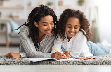 Neşeli anne ve kız evde birlikte çiziyorlar.