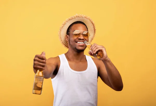 Positiv svart kille i sommar outfit håller två flaskor öl, dricka alkohol dryck på gul studio bakgrund — Stockfoto