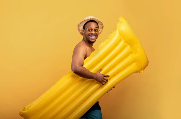 Yüzmek eğlencelidir. Mayolu neşeli siyah adam sarı stüdyo arka planında şişme lilo ile bilardoya gidiyor. — Stok fotoğraf
