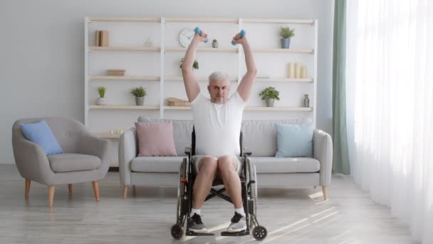 Evde tekerlekli sandalyede oturan dambıllarla egzersiz yapan engelli adam. — Stok video