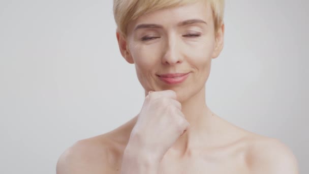 Porträt einer wunderschönen Dame mittleren Alters, die ihre perfekte Gesichtshaut berührt und in die Kamera lächelt, grauer Studiohintergrund — Stockvideo