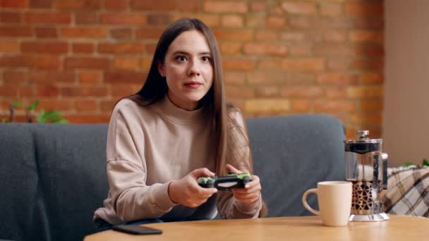 Loisirs domestiques. Jeune femme jouant à des jeux vidéo à la maison, assis sur le canapé avec joystick et se sentant excité à la maison — Video