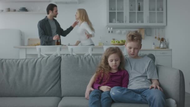 П'яний чоловік з пляшкою сперечається зі своєю плачучою дружиною, двоє нещасних маленьких дітей сидять на дивані, повільний рух, вільний простір — стокове відео