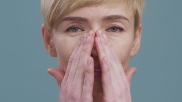 Medelålders dam gör vitalisering ansiktsmassage, smeka hennes ansikte, närbild porträtt, blå studio bakgrund — Stockvideo