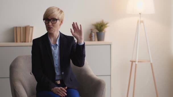 Cheerful middle aged woman psychologist waving hand hello to camera, , greeting patient at light office, free space — Stock Video