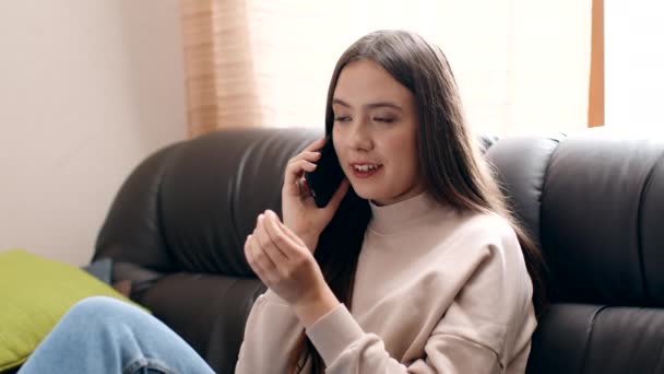 Comunicación móvil. Mujer joven positiva hablando con un amigo a través del teléfono celular, descansando en el sillón en casa — Vídeo de stock