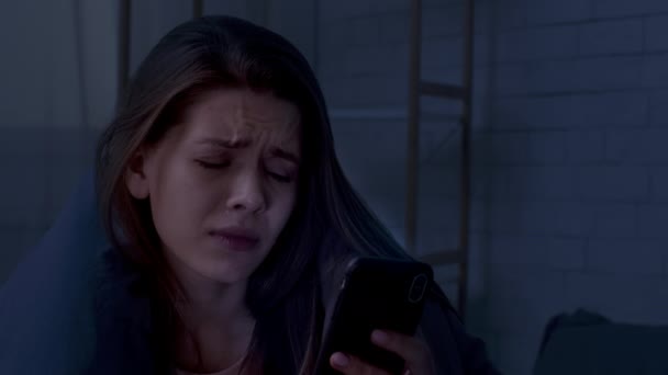 Przygnębiona kobieta trzyma smartfon i płacze cierpiąc z powodu samotności w domu — Wideo stockowe