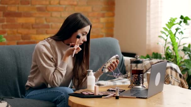 Online make-up cursussen. jonge zelf geïsoleerde vrouw zitten tegen laptop en het toepassen van rouge op haar gezicht — Stockvideo