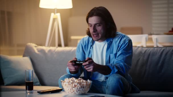 Giovane uomo che gioca ai videogiochi in serata, vincendo e celebrando la sua vittoria, seduto da solo sul divano di casa — Video Stock