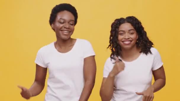 Winnaar dans. Twee gelukkige Afrikaans-Amerikaanse vrouwen vrienden dansen samen, vieren samen de overwinning, oranje achtergrond — Stockvideo