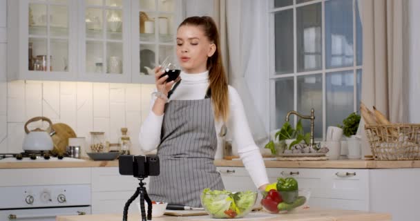 Young housewife wearing apron drinking wine, cheering to smartphone, video chatting with boyfriend at kitchen — Stock Video