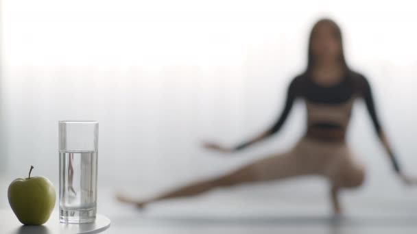 Water en appel liggend op de vloer terwijl Lady doet Yoga — Stockvideo