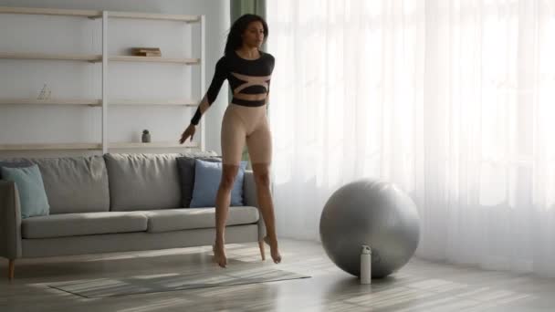 Атлетическая афро-американская женщина делает прыжок Приседания упражнения дома — стоковое видео