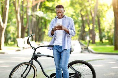 Bisikletli komik siyah adam parkta akıllı telefondan iletişim kuruyor.