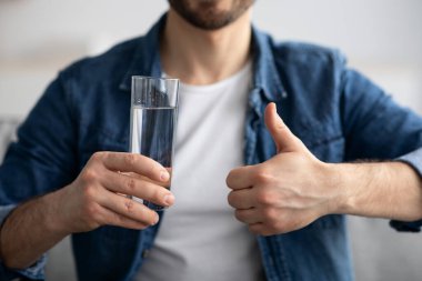 Elinde bir bardak su tutan ve baş parmağını kaldıran tanınmamış bir adam.