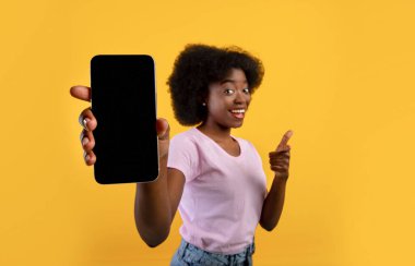 Uygulama ekranı ya da metin için bir model. Afrikalı Amerikalı kadın boş cep telefonu ekranı gösteriyor, sarı arka plan.