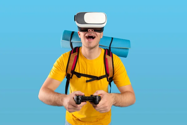 Virtueel reizen. Gelukkige jongeman met VR-headset en joystick op reis avontuur in cyberspace over blauwe achtergrond — Stockfoto