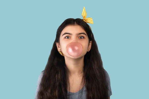 Söt indisk tonåring flicka blåser bubbla från tuggummi, med upphetsad ansikte uttryck över blå bakgrund — Stockfoto