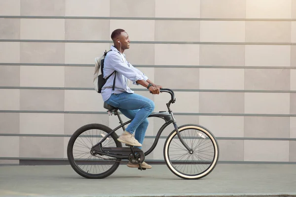 자전거에 이어폰을 달고 자전거를 타고 다니는 멋진 흑인 이 시내 벽돌 벽 근처에 있는 모습 — 스톡 사진