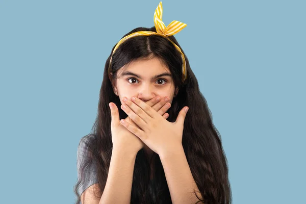 Chocado indiana adolescente menina cobrindo sua boca com as mãos e olhando para a câmera, mantendo o silêncio no fundo azul — Fotografia de Stock