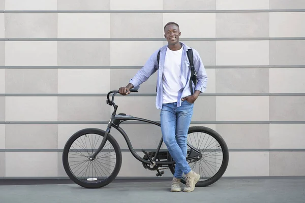 Retrato de comprimento total de cara preto feliz com bicicleta moderna de pé na rua da cidade e olhando para a câmera — Fotografia de Stock