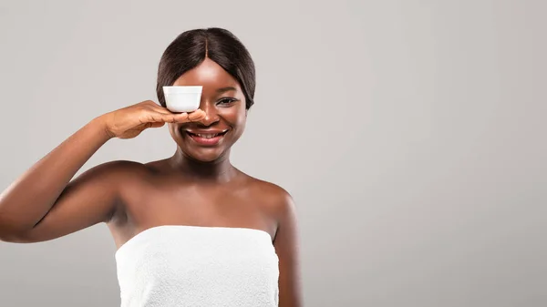 Produtos de beleza. Africano mulher envolto em toalha segurando frasco com creme nutritivo — Fotografia de Stock