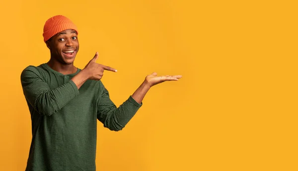 Positieve zwarte man wijzende vinger op open palm, geïsoleerd op gele achtergrond — Stockfoto