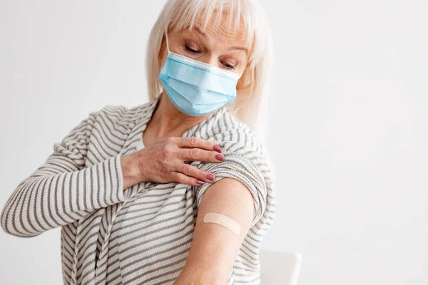 Senior vrouw toont gevaccineerde arm na antivirale injectie, White Studio — Stockfoto