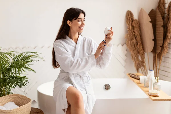 Mujer sosteniendo crema hidratante piel sentada en la bañera en el baño — Foto de Stock