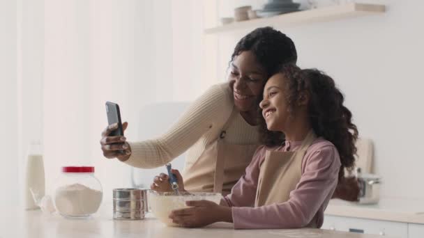 Happy african american mother and daughter making selfie at kitchem, smiling to smartphone while cooking bakery together — Stock Video