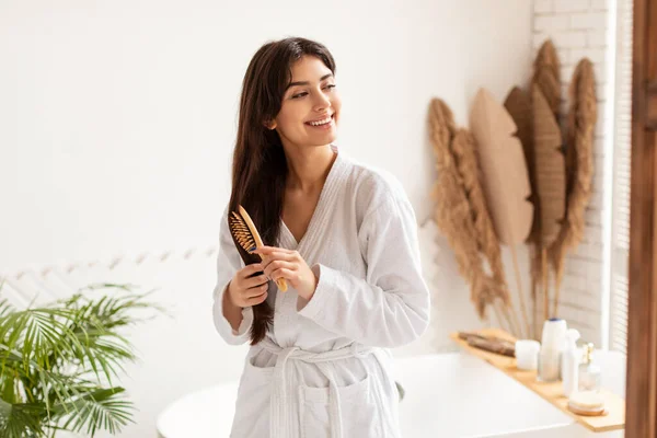 Morena mujer cepillando el cabello con cepillo de madera en el baño moderno — Foto de Stock