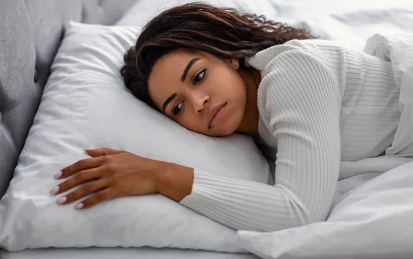 Θλιβερή μαύρη γυναίκα ξαπλωμένη στο κρεβάτι μόνη και αδύναμη αναστατωμένη. — Φωτογραφία Αρχείου