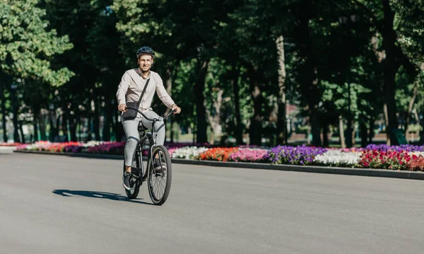 Jovem funcionário alegre com capacete em passeios de bicicleta utilitária para o local de trabalho moderno — Fotografia de Stock