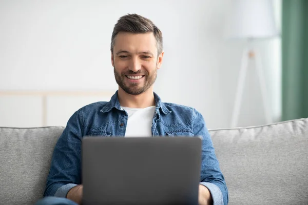 Gros plan de l'homme barbu positif en utilisant un ordinateur portable à la maison — Photo