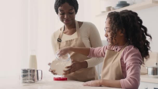 Bakery preparations. Cute little black girl flouring tabletop at kitchen, cooking cookies with mother together — ストック動画