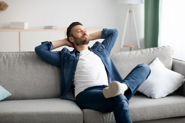 Щасливий бородатий чоловік розслабляється на дивані вдома — стокове фото