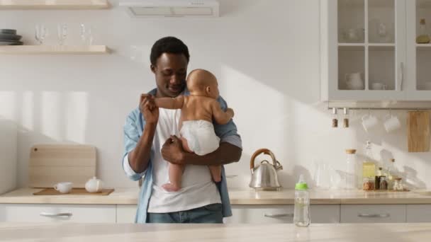Happy african american father lullying his newborn baby in diaper, dancing with toddler at kitchen interior, slow motion — Stock videók