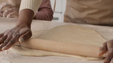 Close up shot of african american woman rolling out dough and little girl cutting cookies with metal cutter, slow motion