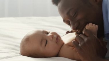 Close up of happy smiling african american man enjoying his fatherhood, embracing and playing with his newborn baby