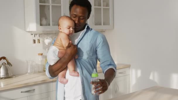 Water balance. African american father carrying newborn baby, coming to kitchen and giving baby bottle to thirsty kid — Stock video