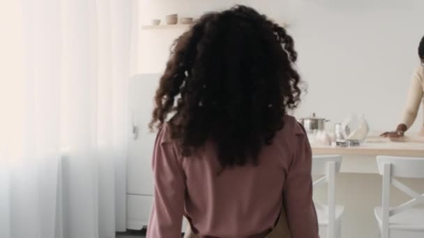 Follow shot of african american girl going to mother and helping her, adding flour to dough at kitchen, slow motion — Wideo stockowe