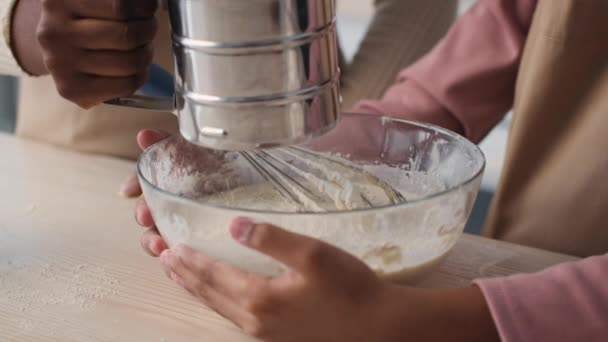 閉じるアップの小さな黒の女の子調理ペストリーとともに母,女性追加小麦粉と娘泡立て器生地でキッチン — ストック動画