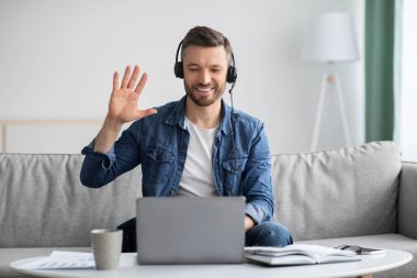 Gülümseyen adam iş görüşmesi yapıyor, kulaklık ve dizüstü bilgisayar kullanıyor.