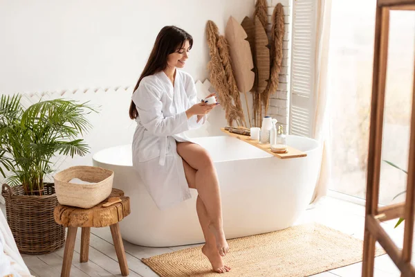 Mujer atractiva aplicando crema hidratante para el cuidado de la piel en el baño —  Fotos de Stock