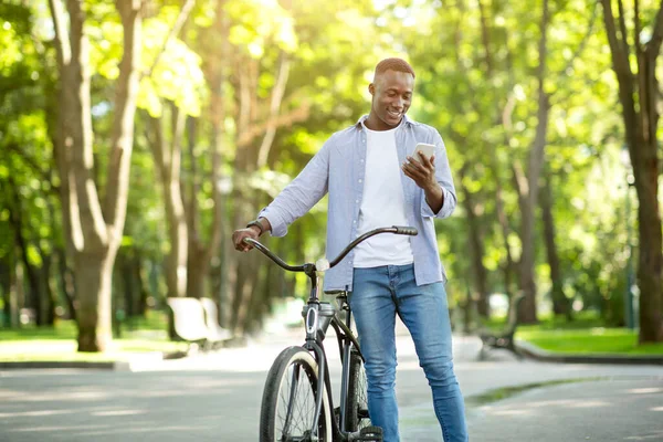 Funky chico afroamericano con bicicleta charlando en el teléfono inteligente al aire libre, espacio para el texto — Foto de Stock