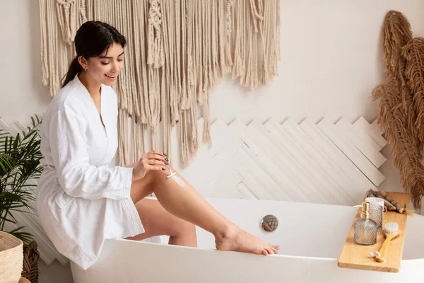 Vrouw scheren benen met scheermes zit op bad in de badkamer — Stockfoto