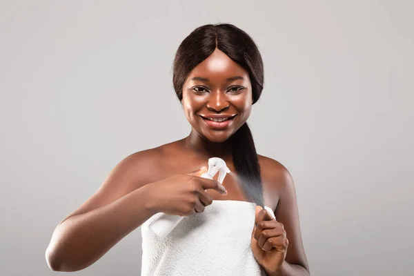 Щоденний догляд за волоссям. Портрет усміхненої афроамериканки, що застосовує зволожуючий спрей для волосся — стокове фото