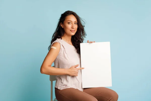Geimpfte Frau hält leere Papiertafel vor blauem Hintergrund — Stockfoto