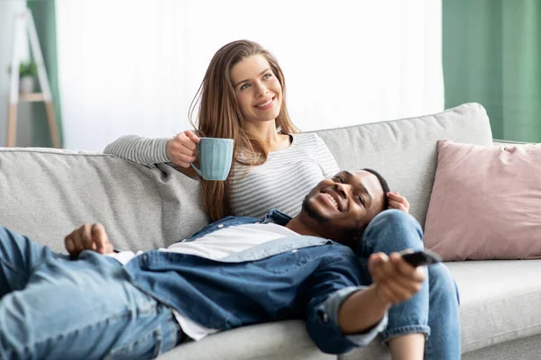 回家的时间。不同种族的夫妻快乐地在客厅的沙发上放松一下 — 图库照片