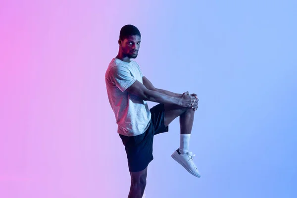 Ayağını neon ışıkta geren atletik siyahi bir adamın portresi. Sağlıklı yaşam tarzı kavramı — Stok fotoğraf